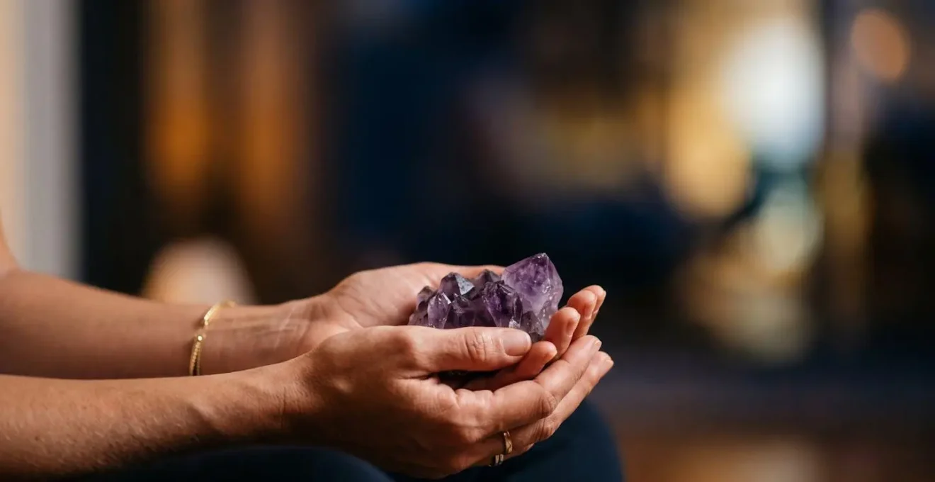 Manos sosteniendo suavemente piedra de amatista durante práctica de reflexión nocturna en ambiente sereno
